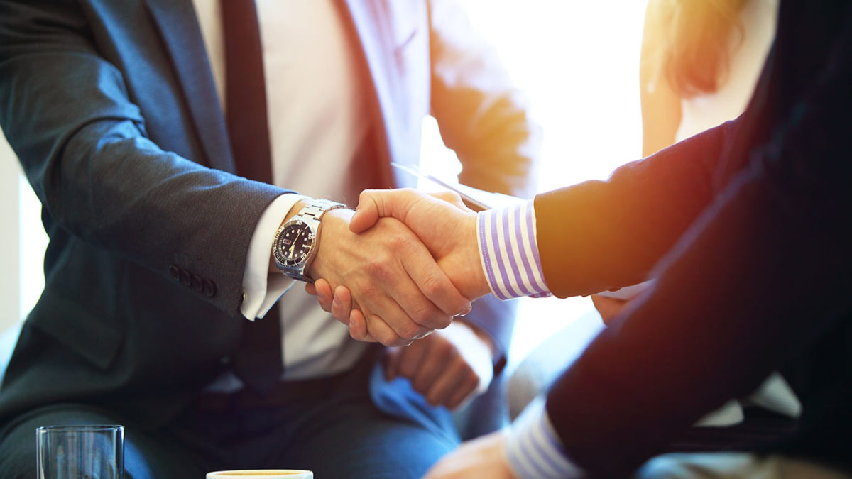 Two people wearing nice business suits shake hands. One of them is wearing a nice watch.