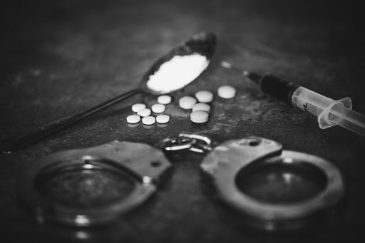 Handcuffs and drugs are seen in a black and white photo