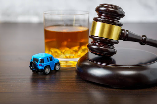 A toy car sits next to what looks to be a straight bourbon. There is also a judge's gavel on the table.